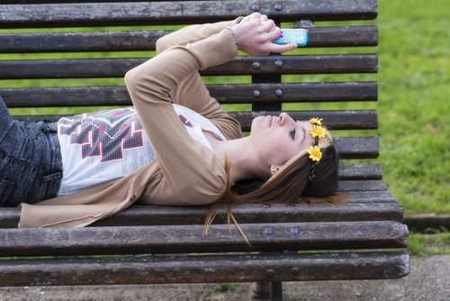 Happines beautiful girl with smart phone lying on the bench.