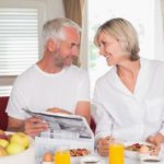 Mature couple reading newspaper while having breakfast at home