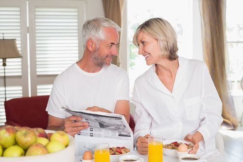 Mature couple reading newspaper while having breakfast at home