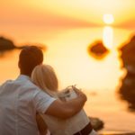 couple sitting and watching the sun on the beach at sunrise