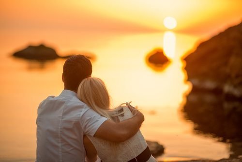 couple sitting and watching the sun on the beach at sunrise